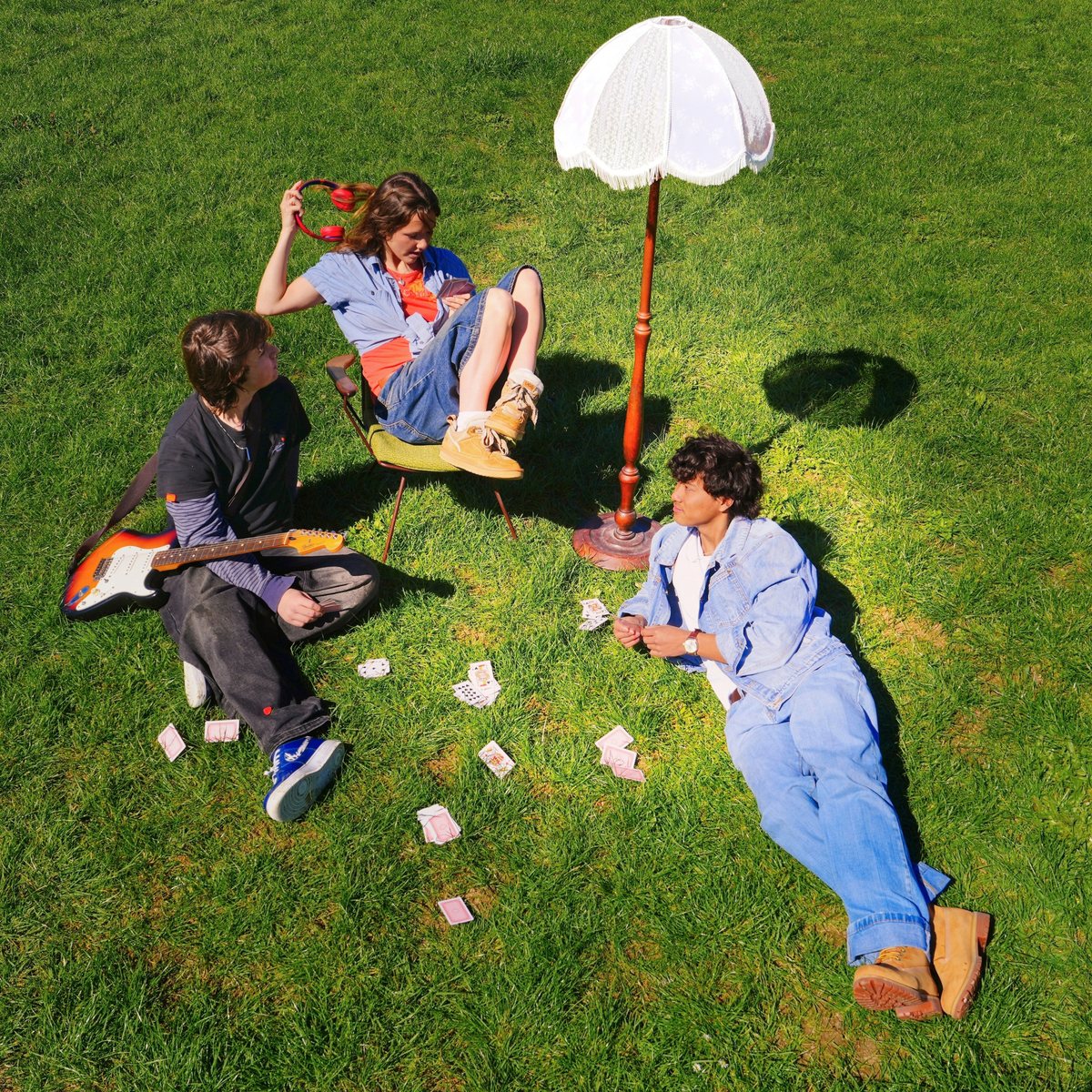 Juna on the grass with a standing lamp and scattered playing cards: artwork for the EP &lsquo;she&rsquo;s coming over again&rsquo;